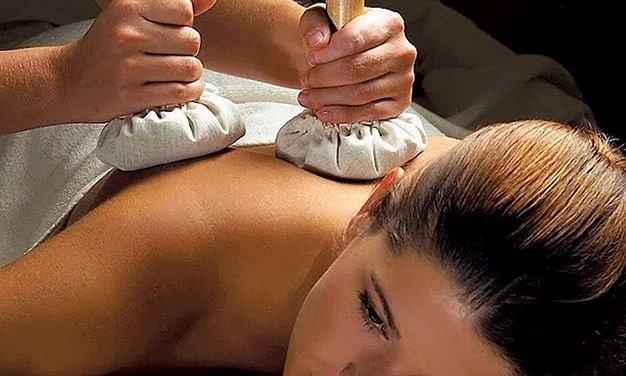 Therapist preparing herbal boluses for Kizhi treatment at Pranavam Ayurveda Hospital